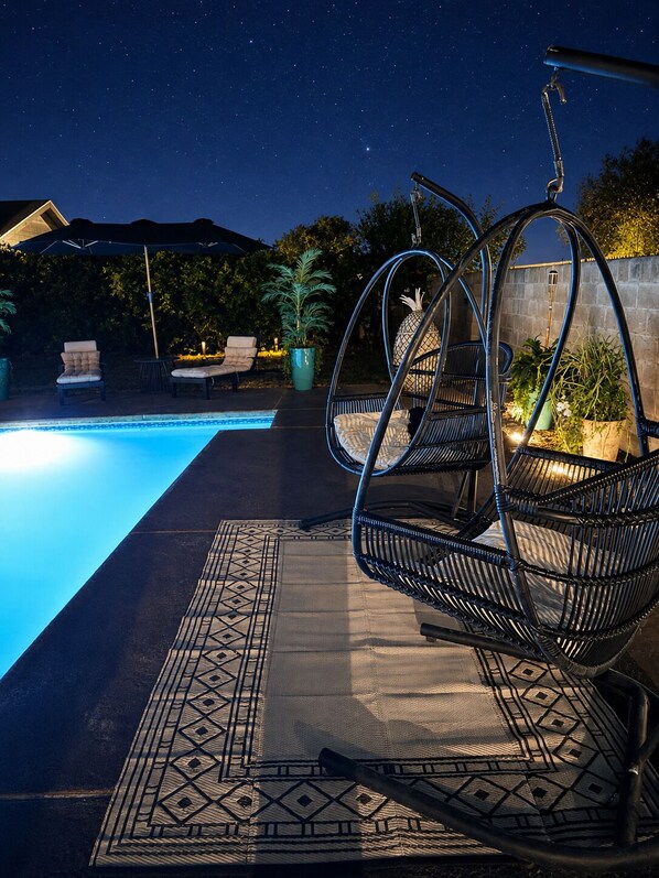 A poolside area with a hanging chair, a patterned rug, and a potted plant.