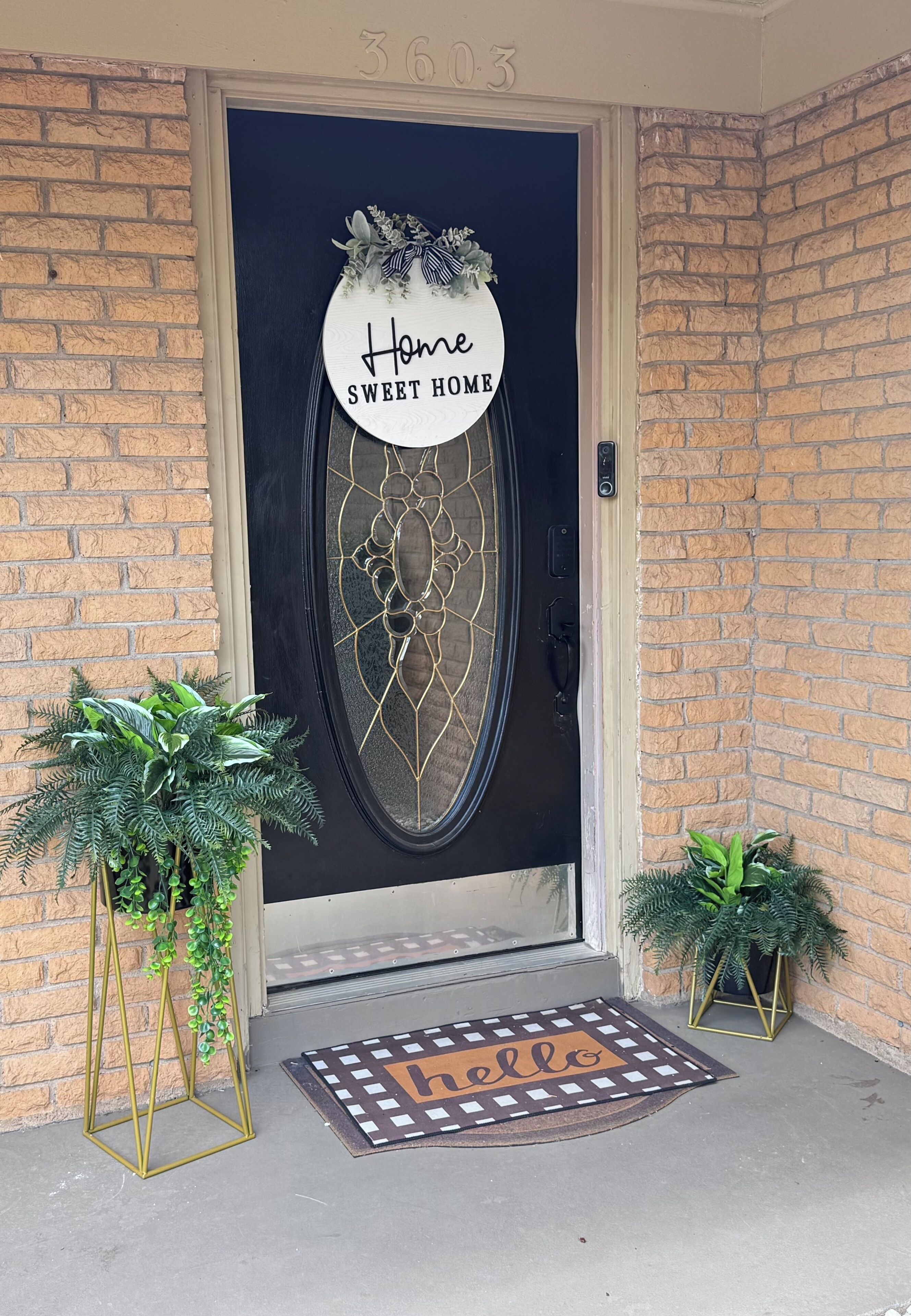 A front door with a decorative glass panel, a welcome mat, and two potted plants.
