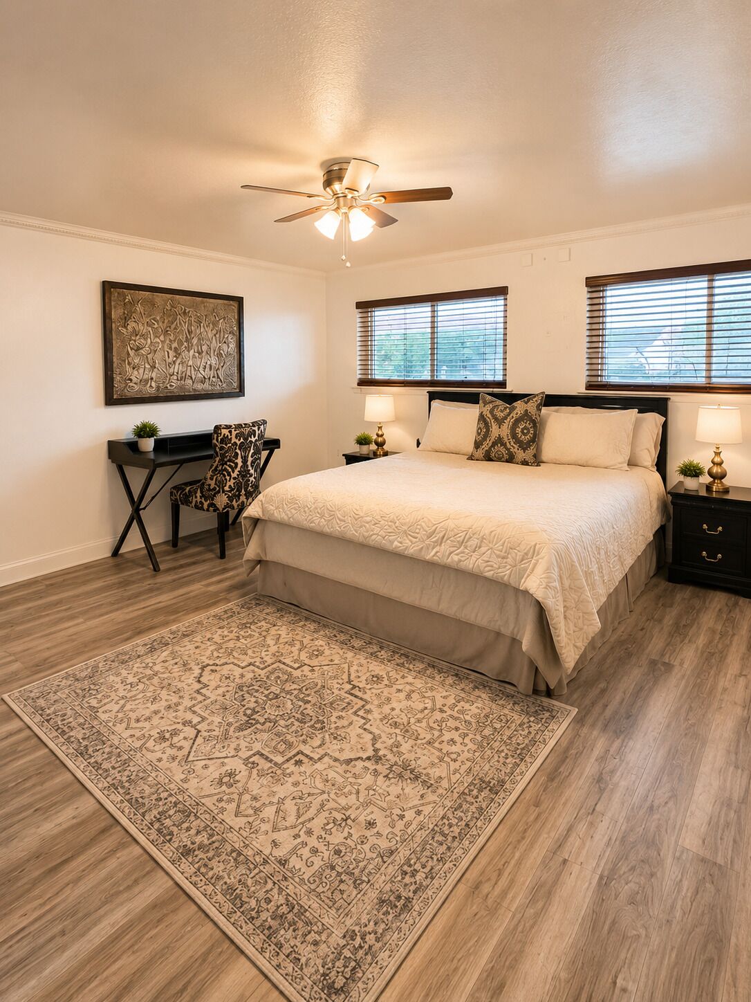 A bedroom with a bed, bedside tables, a desk, a chair, a rug, and a ceiling fan.