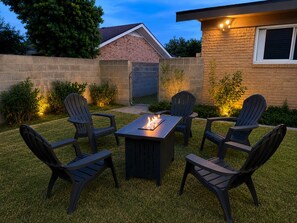 A patio with a fire pit table and four Adirondack chairs.