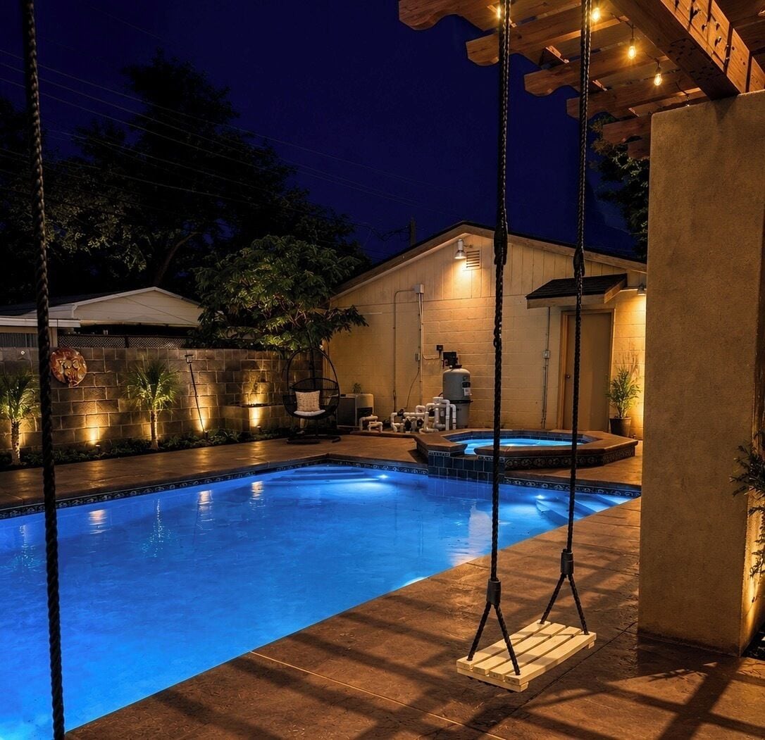 A swimming pool with a hot tub, surrounded by a patio with outdoor furniture and a wooden swing set.