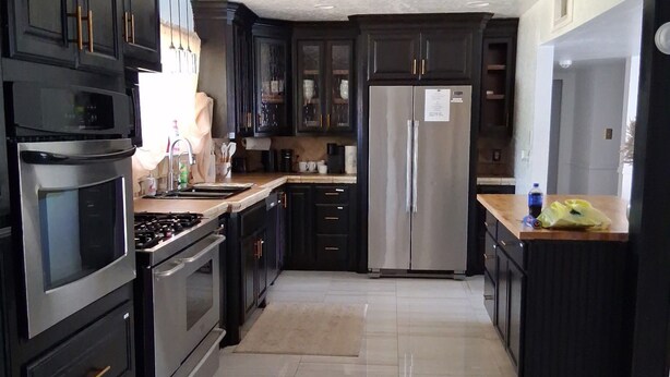 A modern kitchen with dark cabinetry, stainless steel appliances, and a tiled floor. - Maple Estate Private Pool, Hot Tub & Resort-Style Backyard (Odessa)