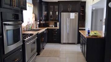 A modern kitchen with dark cabinetry, stainless steel appliances, and a tiled floor.