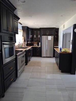 A modern kitchen with dark cabinetry, stainless steel appliances, and a tiled floor.