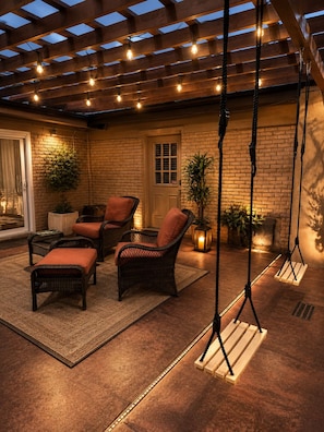 An outdoor patio with wicker furniture, a swing set, and a brick wall. - Maple Estate Private Pool, Hot Tub & Resort-Style Backyard (Odessa)