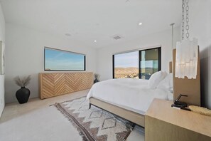 A modern bedroom with a large bed, a wooden cabinet, a large window with a desert view, and a hanging light fixture. - Sagebrush Hideaway Pool, Sauna, Cold Plunge, Views (Pioneertown)