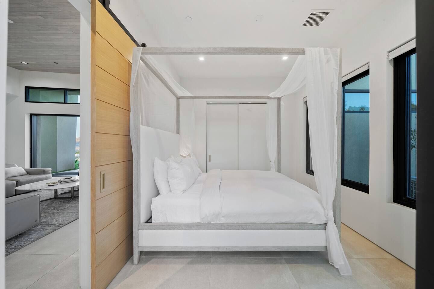 Une chambre moderne avec un lit à baldaquin, de grandes fenêtres et une vue sur l’extérieur.