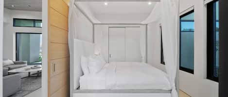 Une chambre moderne avec un lit à baldaquin, de grandes fenêtres et une vue sur l’extérieur.