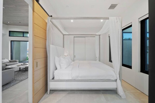 A modern bedroom with a canopy bed, large windows, and a view of the outdoors.