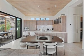 A modern kitchen with a central island, built-in appliances, and a dining area with a table and chairs. - Sagebrush Hideaway Pool, Sauna, Cold Plunge, Views (Pioneertown)