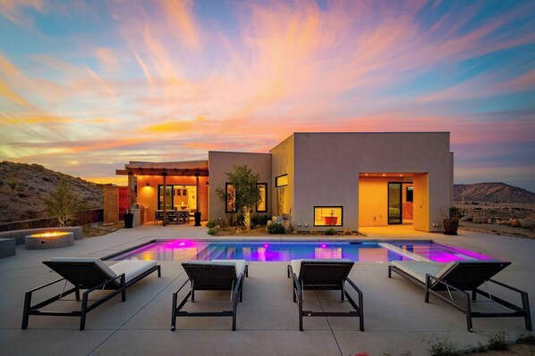 A modern house with a pool, outdoor seating, and a sunset view.