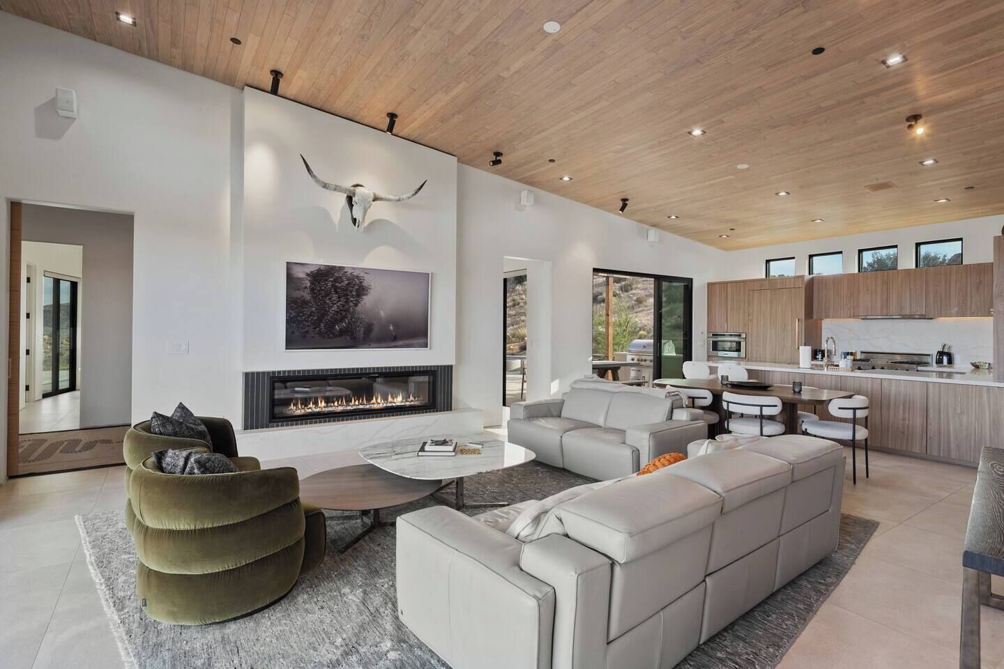 A modern living room with a fireplace, a large sofa, and a dining area with a kitchen in the background.