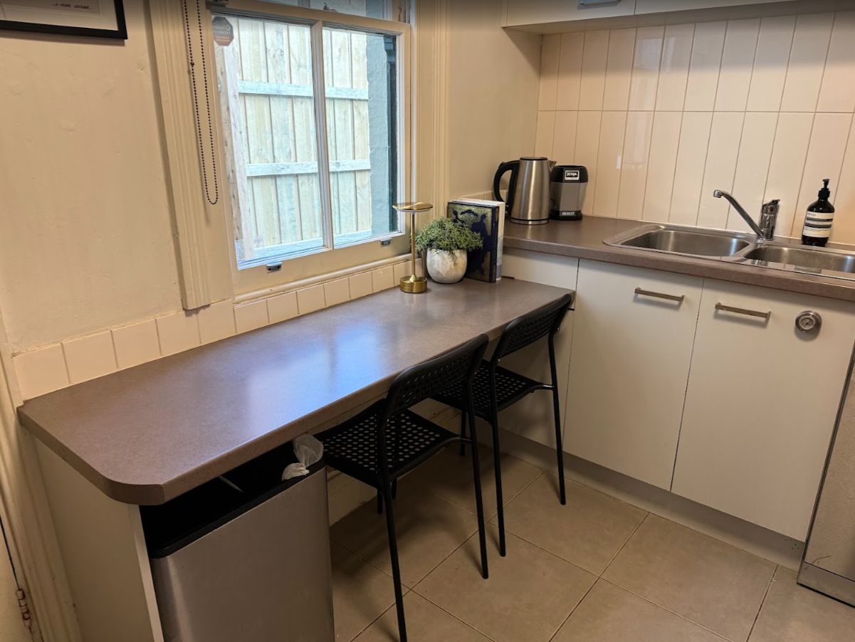 A kitchen with a countertop, two chairs, a sink, cabinets, and a window.