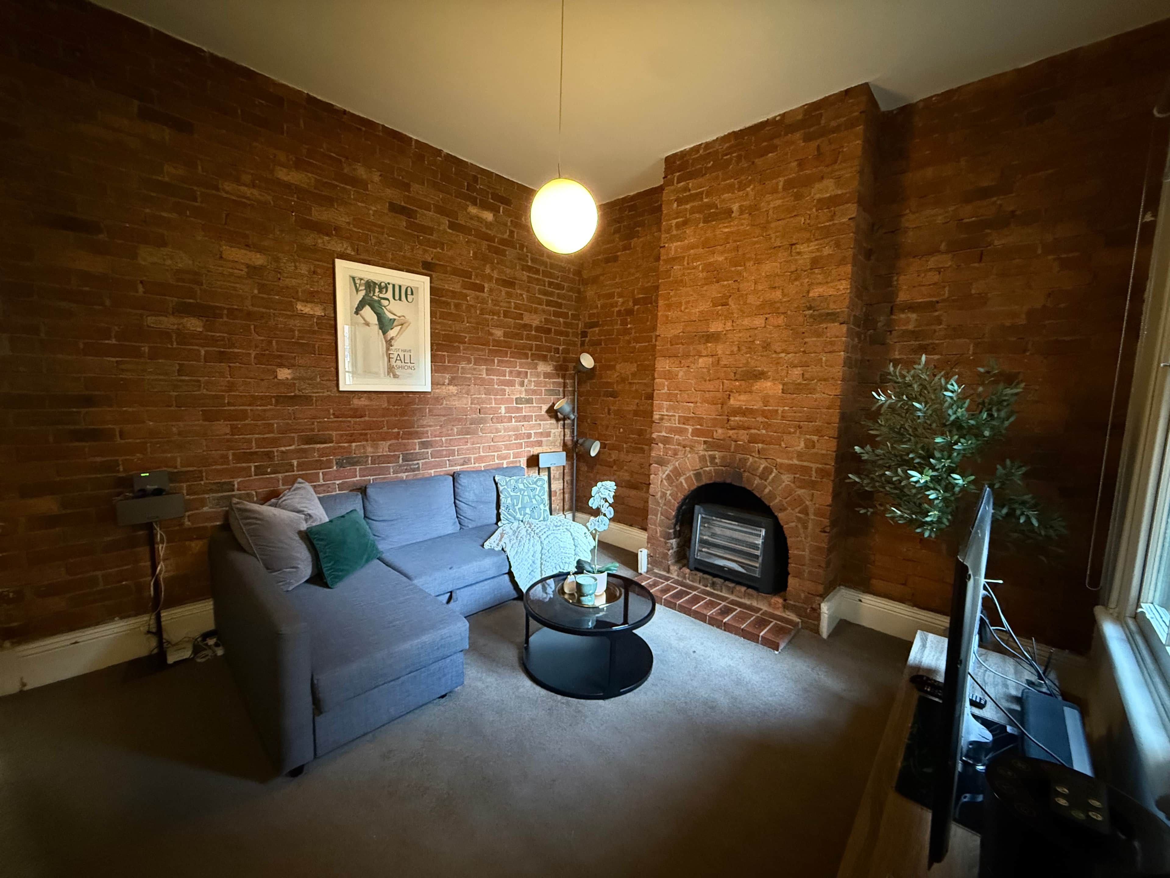 A living room with a brick wall, a sofa, a coffee table, a fireplace, and a television.