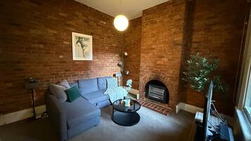 A living room with a brick wall, a sofa, a coffee table, a fireplace, and a television.