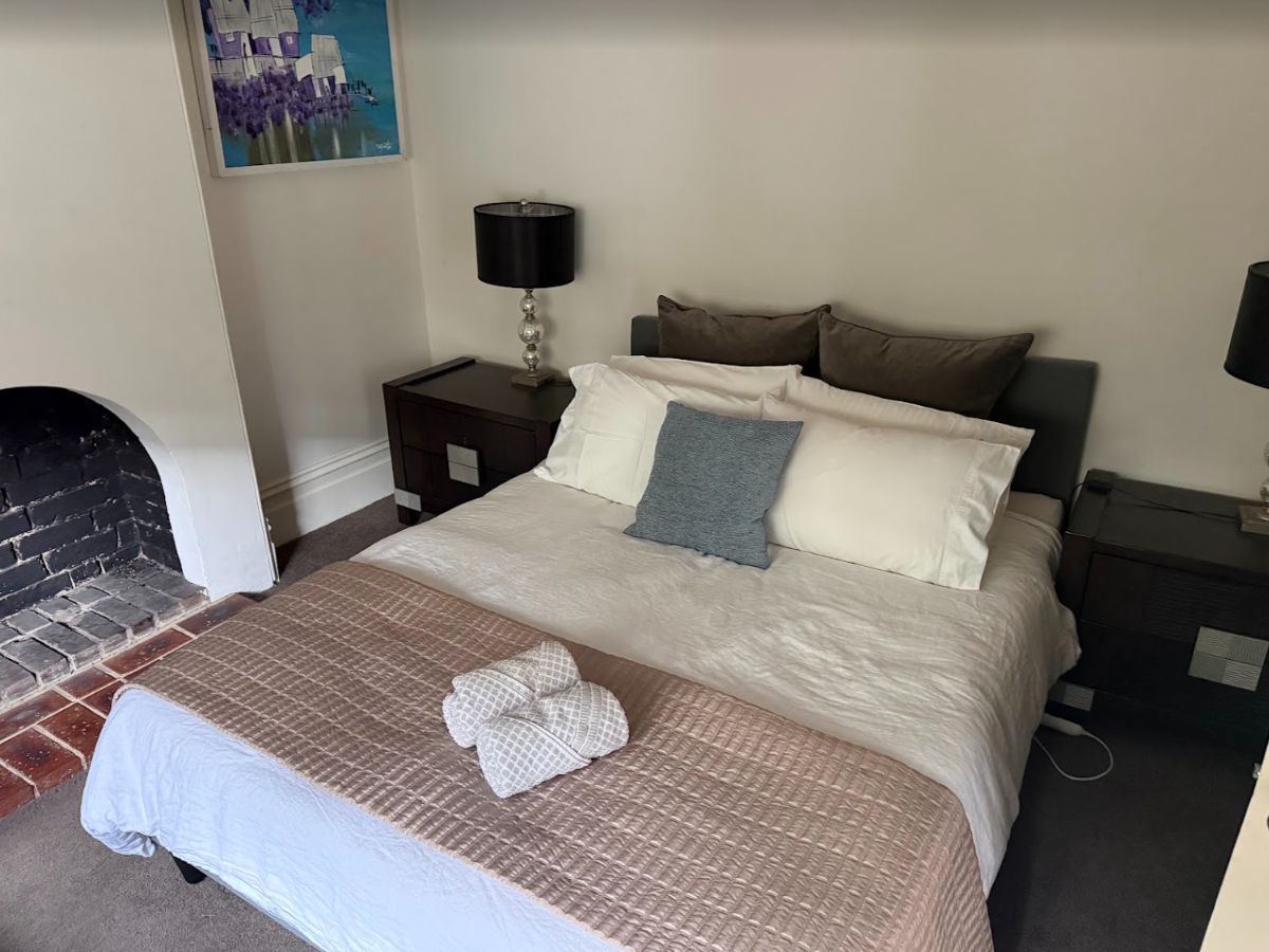 A neatly made bed with a patterned bedspread and pillows, a bedside table with a lamp, and a painting on the wall.