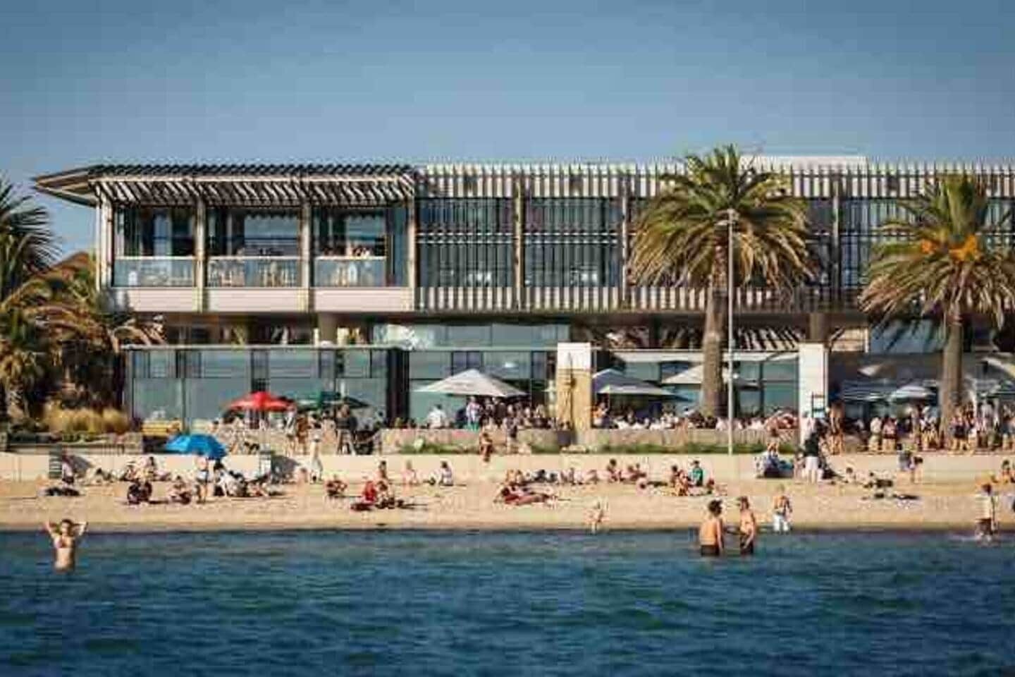 A beachfront hotel with a pool, palm trees, and a crowd of people.