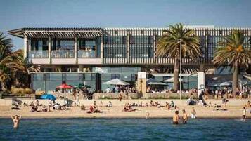 A beachfront hotel with a pool, palm trees, and a crowd of people.
