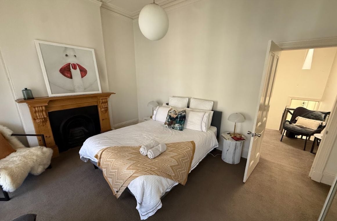 A bedroom with a bed, a fireplace, a door leading to another room, and a chair.