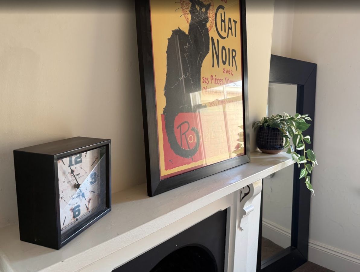 A framed poster with a cat and text, a clock, and a plant on a shelf.