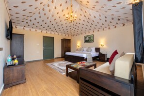 A hotel room with a bed, a sofa, a coffee table, a TV, and a wardrobe. - Sterling Leopard Haven Jawai (Bali)