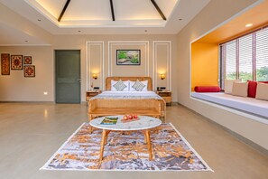 Une chambre d’hôtel comprenant un lit, des tables de chevet, un coin lecture avec une table et des chaises, une fenêtre donnant sur un paysage agréable et une porte.