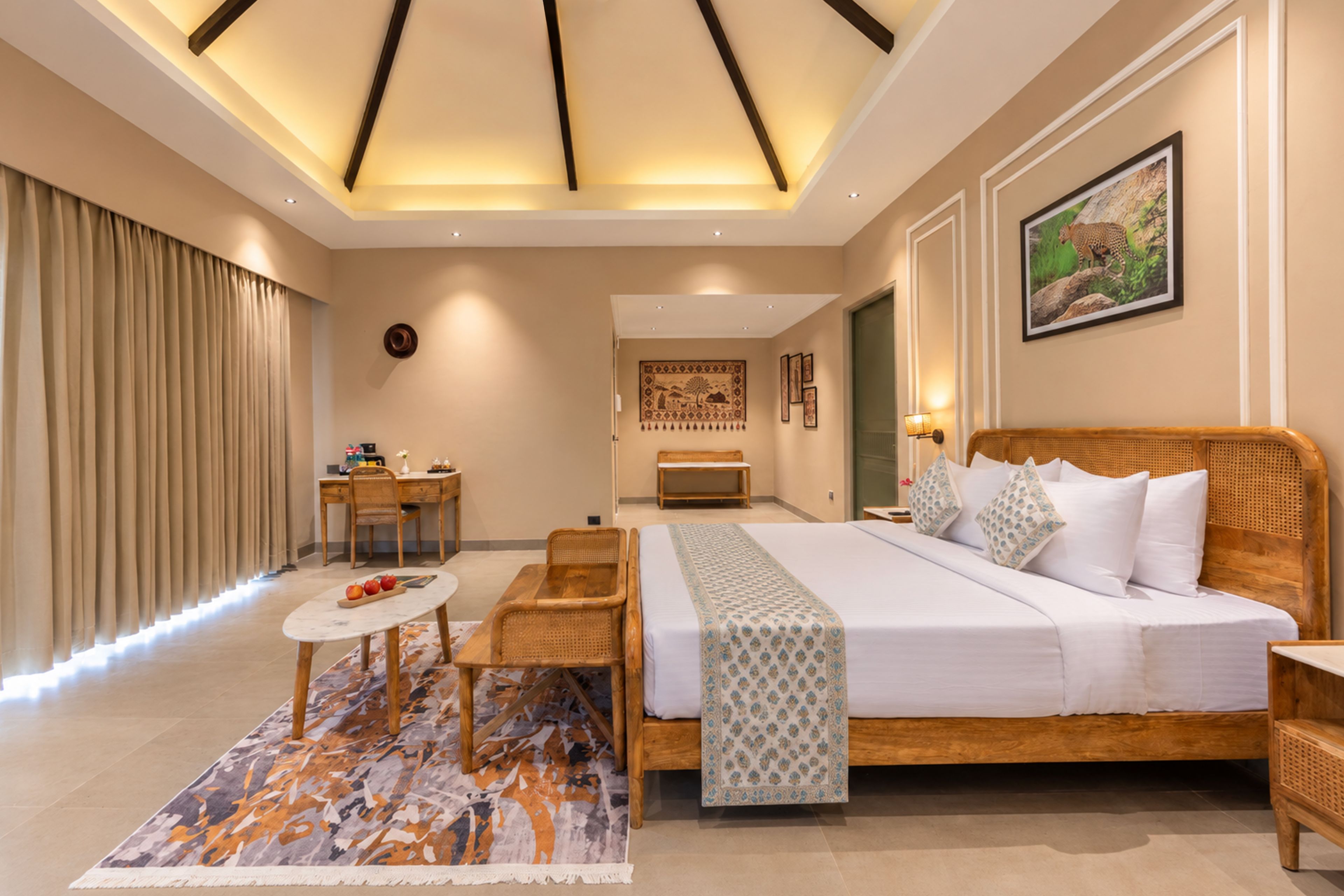 A hotel room with a large bed, a desk, a chair, a small table, and a patterned rug.