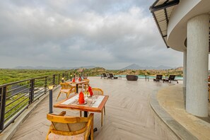 An outdoor dining area with tables and chairs, overlooking a landscape with greenery and distant mountains. - Sterling Leopard Haven Jawai (Bali)