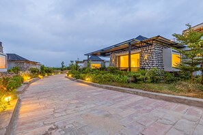 Un sendero conduce a una hilera de casas modernas con fachadas de piedra y grandes ventanales, rodeado de vegetación.