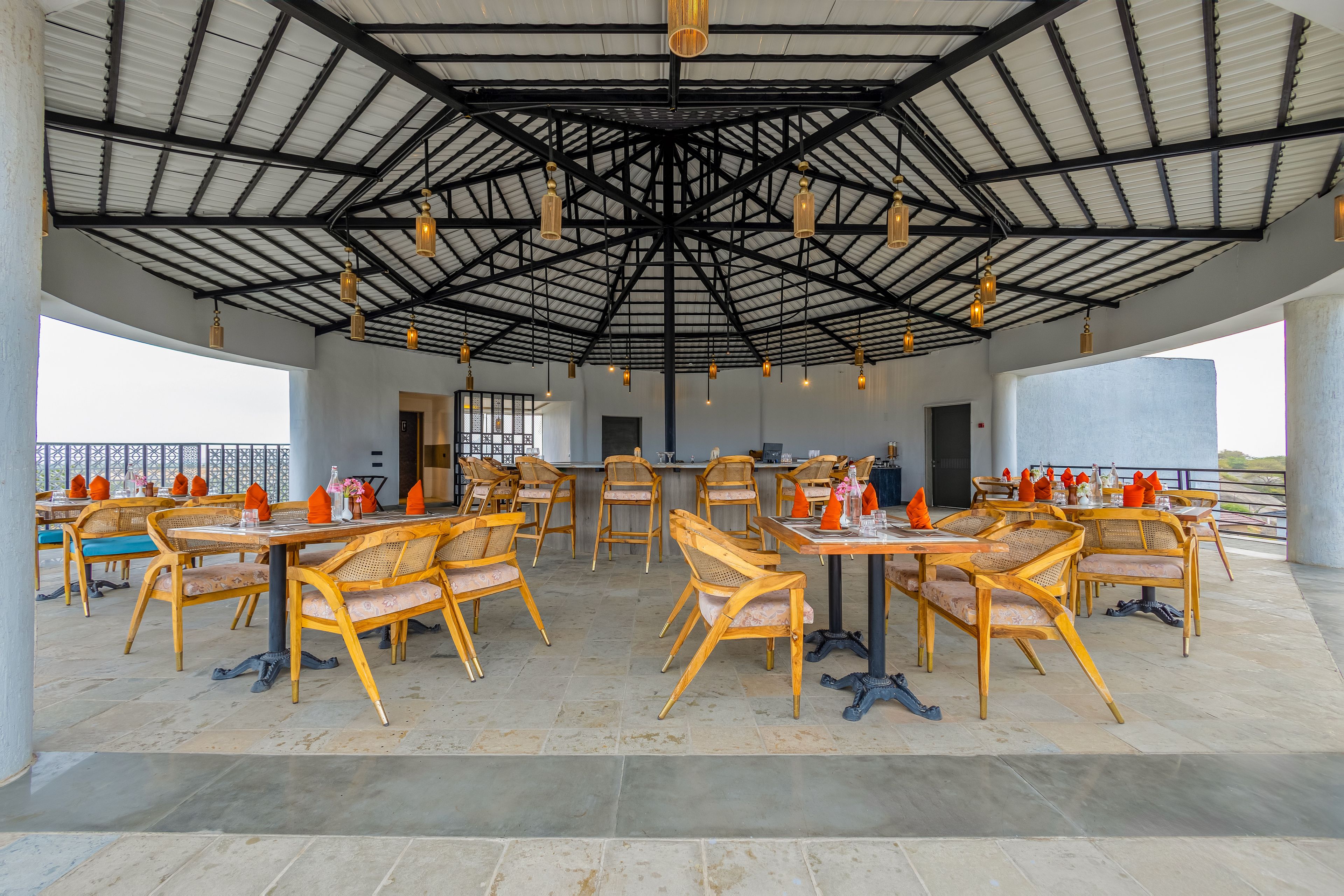 An outdoor dining area with multiple tables and chairs, a covered roof structure, and a view of the surrounding landscape.