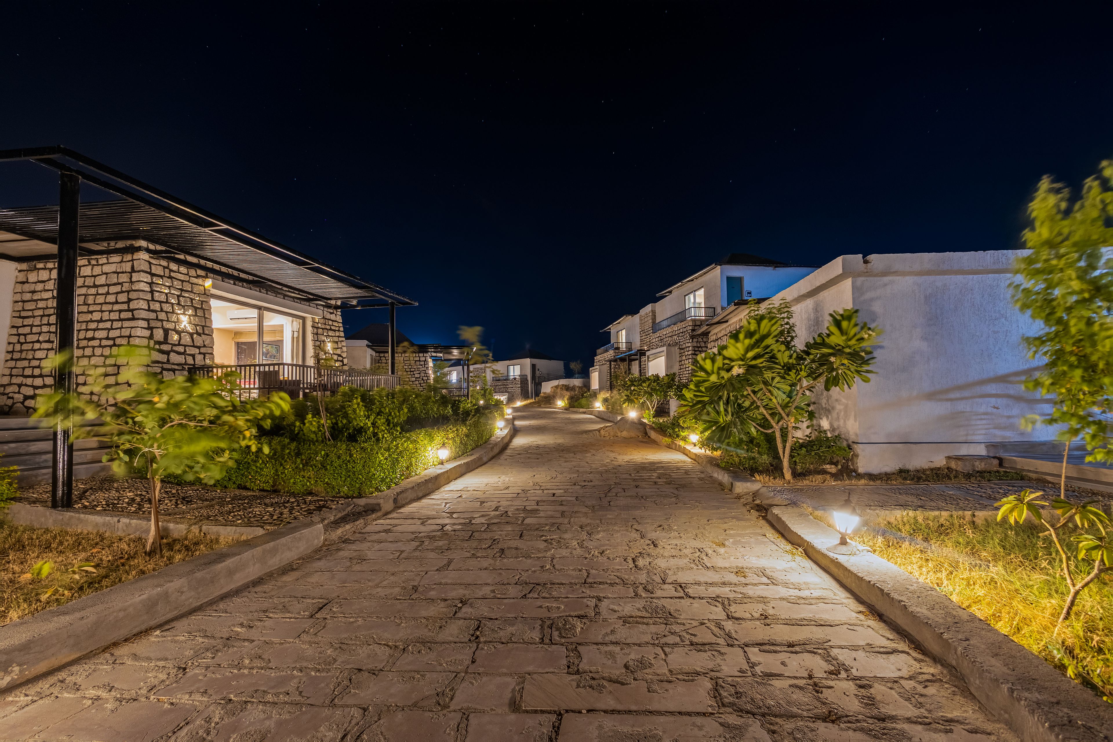A nighttime street view with stone-paved sidewalks, residential buildings, and illuminated outdoor lighting.