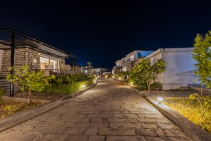 Vista nocturna de una calle con aceras empedradas, edificios residenciales e iluminación exterior.
