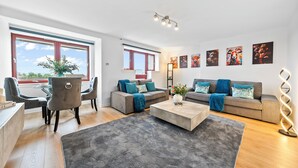 A modern living room with a sofa set, a coffee table, and a dining area with chairs and a table. - 3 bed Modern Apartment near Glasgow city Centre,Glasgow airport and Loch Lomond (Clydebank)