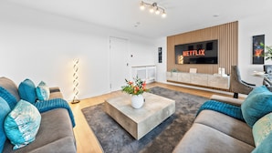 A modern living room with a flat-screen TV, a coffee table with flowers, and a sofa with decorative pillows. - 3 bed Modern Apartment near Glasgow city Centre,Glasgow airport and Loch Lomond (Clydebank)