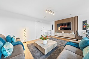 A modern living room with a flat-screen TV, a coffee table with flowers, and a sofa with decorative pillows. - 3 bed Modern Apartment near Glasgow city Centre,Glasgow airport and Loch Lomond (Clydebank)