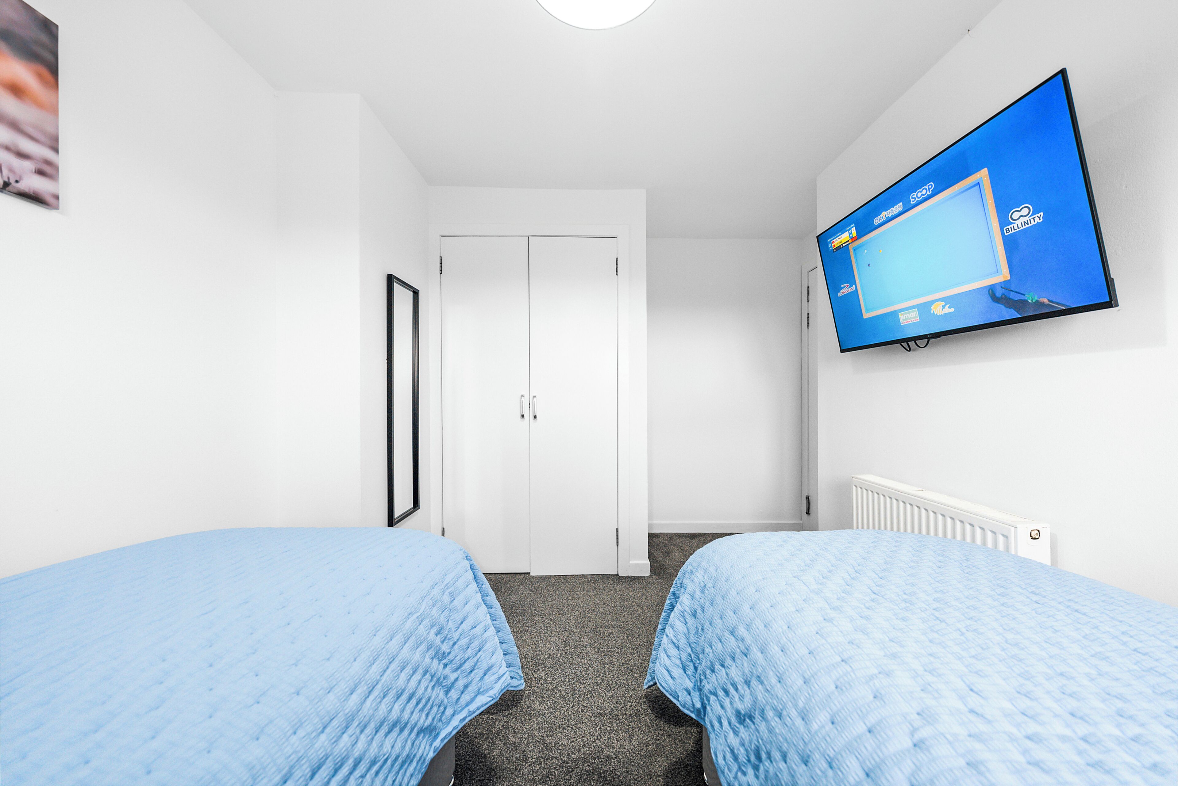 A hotel room with two beds, a television mounted on the wall, and a white door.