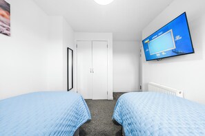 Habitación de hotel con dos camas, un televisor montado en la pared y una puerta blanca.