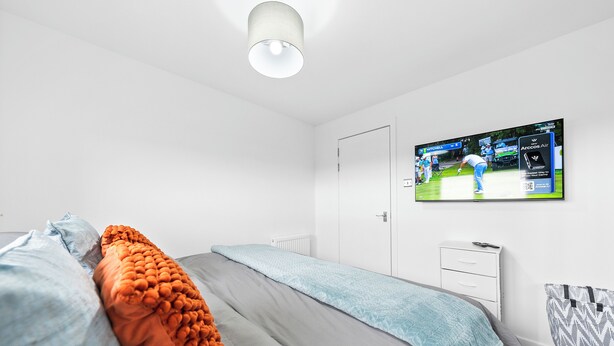 A bedroom with a bed, a television mounted on the wall, and a door. - 3 bed Modern Apartment near Glasgow city Centre,Glasgow airport and Loch Lomond (Clydebank)