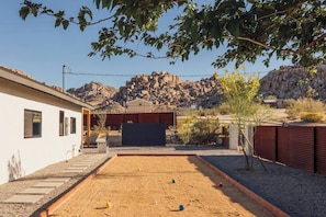A courtyard with a sand court, a building with a garage, and a rocky mountain backdrop. - Pool, Hot Tub, Stars, Views, Yoga Pad, Bocce, BBQ (Joshua Tree)