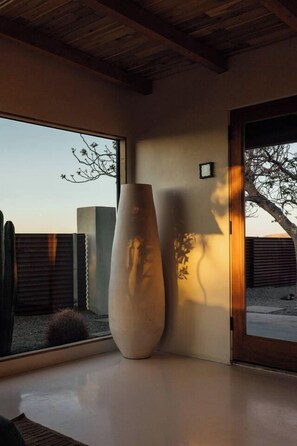 A room with a large window, a tall vase, and a door leading outside. - Pool, Hot Tub, Stars, Views, Yoga Pad, Bocce, BBQ (Joshua Tree)