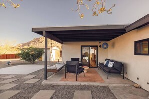 A modern outdoor patio with a swing, seating area, and a view of a mountain. - Pool, Hot Tub, Stars, Views, Yoga Pad, Bocce, BBQ (Joshua Tree)