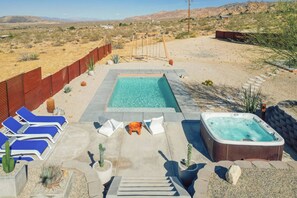 A pool area with a hot tub, lounge chairs, and a wooden swing set.
