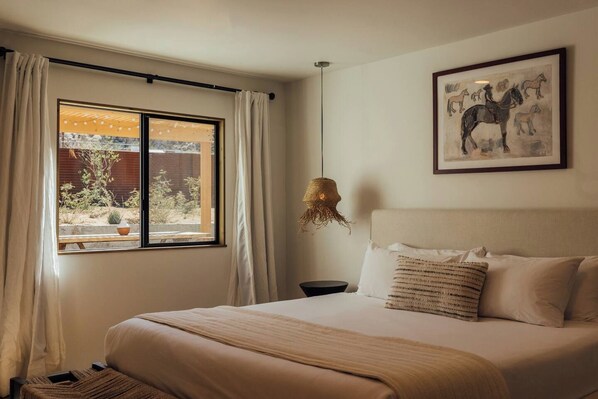 A bedroom with a bed, a window with curtains, a hanging light fixture, and a framed picture on the wall.