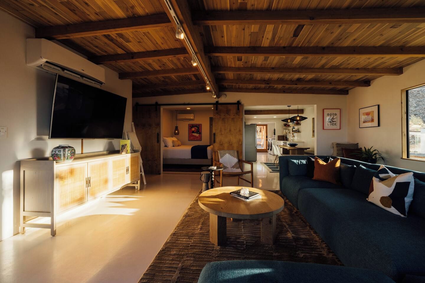 Una sala de estar moderna con techo de madera, televisor, sofá y comedor.