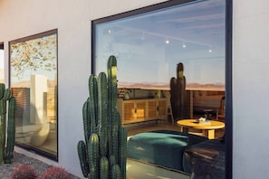 A modern interior with a large window, a cactus plant, a sofa, and a table. - Pool, Hot Tub, Stars, Views, Yoga Pad, Bocce, BBQ (Joshua Tree)