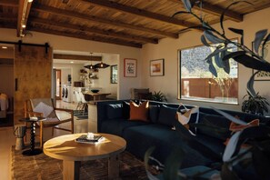 A modern living room with a dark blue sofa, a round wooden coffee table, and a dining area with a kitchen in the background.
