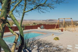 A swimming pool with a wooden swing set and a view of distant mountains. - Pool, Hot Tub, Stars, Views, Yoga Pad, Bocce, BBQ (Joshua Tree)