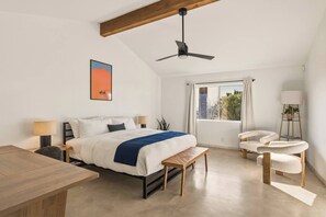 A modern bedroom with a bed, bedside tables, a desk, a chair, a standing lamp, and a ceiling fan.