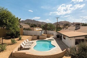 A residential backyard with a swimming pool, lounge chairs, and a view of mountains.