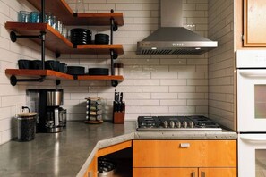 A kitchen with wooden shelves, a coffee maker, a spice rack, and a stove.